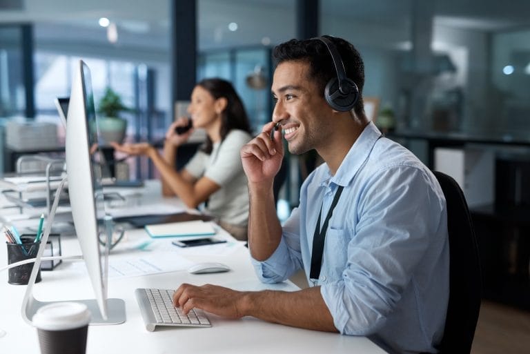 Dedicated service creates dedicated customers. Shot of a young man using a headset and computer in a modern office.
